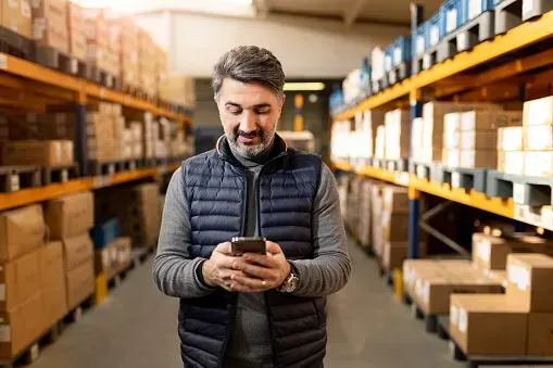 Warehouse worker checking a smartphone between storage shelves