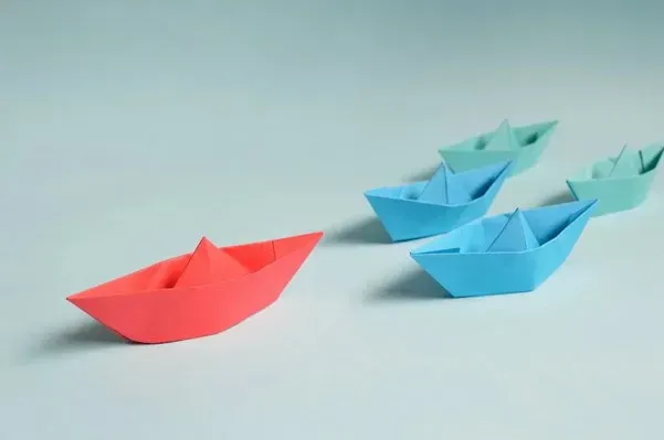 Red paper boat leading a group of blue paper boats