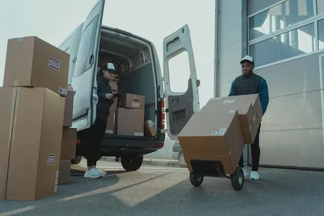 Delivery workers moving boxes between a van and a hand truck