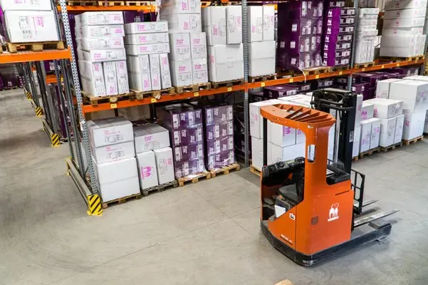 Forklift beside palletized stock on warehouse shelves