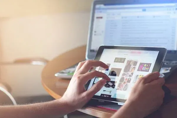 Person browsing products on a tablet beside a laptop