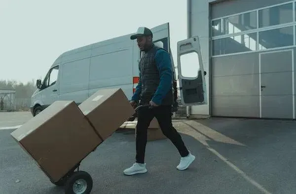 Delivery worker moving boxes on a hand truck beside a van