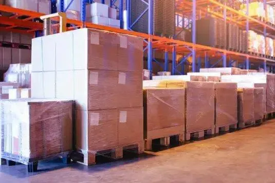 Shrink-wrapped boxes on pallets beside warehouse racks
