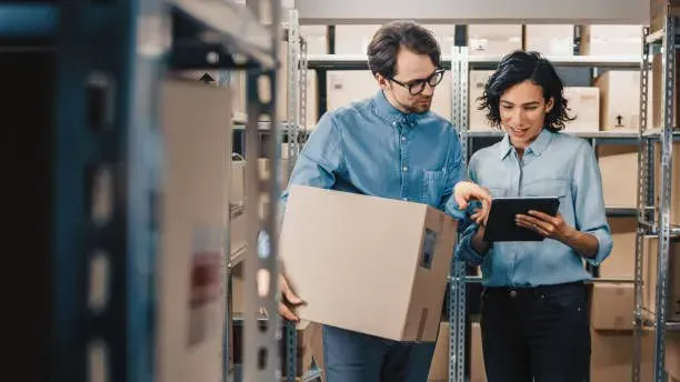 Two warehouse workers checking a box against information on a tablet