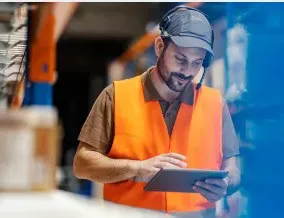 Warehouse worker wearing a safety vest and checking a tablet